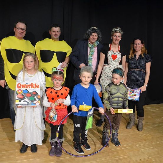 Eine Gruppe von Menschen posiert für ein Foto. Einige tragen Kostüme und halten Spielzeug. Ein Junge im Hulk-Kostüm hält eine Hula-Hoop. Hinter ihnen ist ein schwarzer Hintergrund.