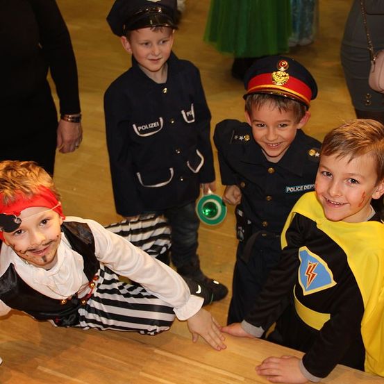 Vier junge Jungen, die in Kostümen gekleidet sind, einer als Pirat, ein anderer als Polizist und zwei weitere in Superhelden-Outfits, posieren für ein Foto in einem Raum.