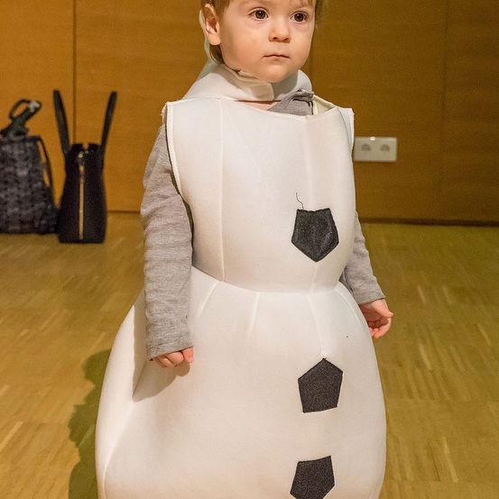 Ein junger Junge, der einen weißen Schneemann-Kostüm mit schwarzen Akzenten trägt, steht in einem Raum.
