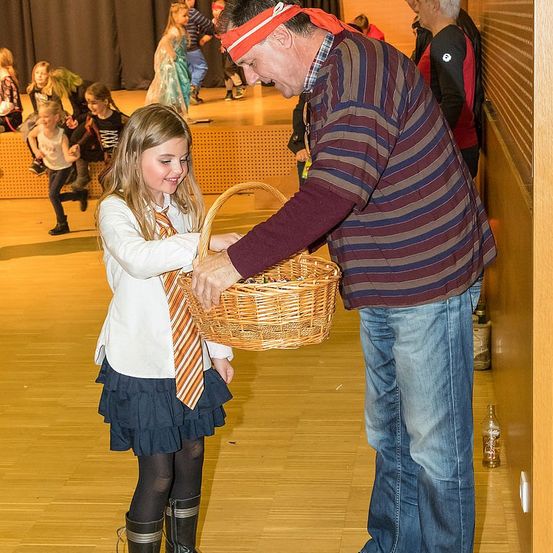 Ein Mann in einem gestreiften Hemd gibt einer jungen Frau, die eine Krawatte trägt, einen Korb in einem Schulkorridor.