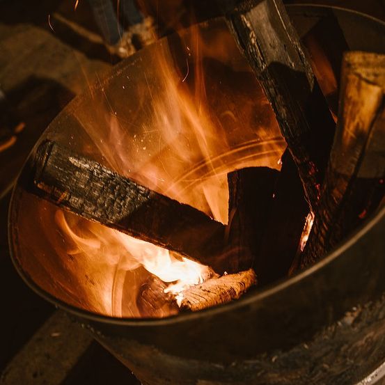 Eine Nahaufnahme eines Feuerkorbs mit brennendem Holz, das ein warmes Licht und Funken abgibt.