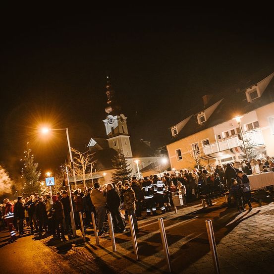 Bei Nacht versammelt sich eine Menschenmenge vor einer Kirche, mit Feuerwehrleuten und einem Tisch mit Kerzen.