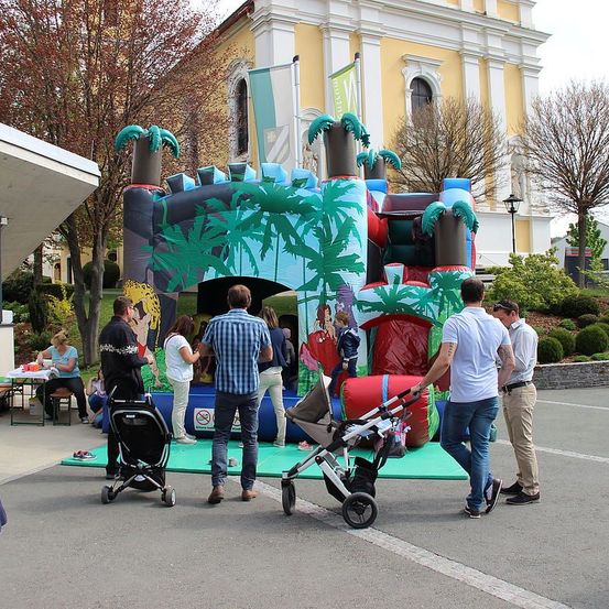 Eine Gruppe von Menschen mit Kinderwagen steht um ein riesiges aufblasbares Schloss mit Palmen im Freien.