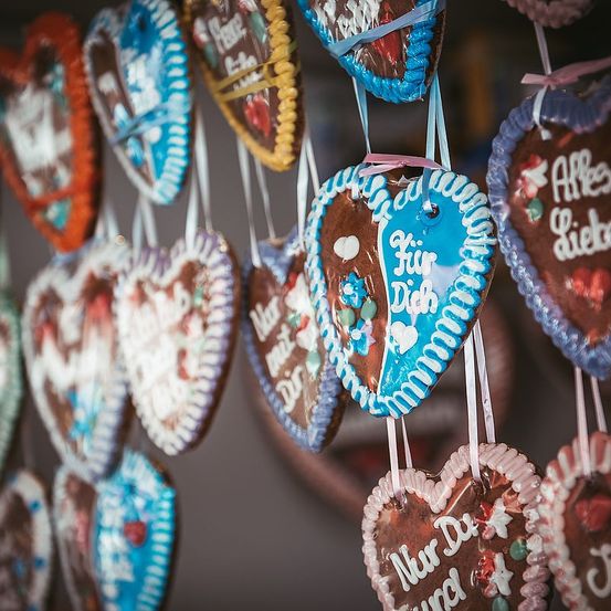 Viele herzförmige Lebkuchen hängen an Fäden. Die Kekse sind mit Zuckerguss und Streuseln verziert. Einige Kekse haben Nachrichten auf Deutsch.