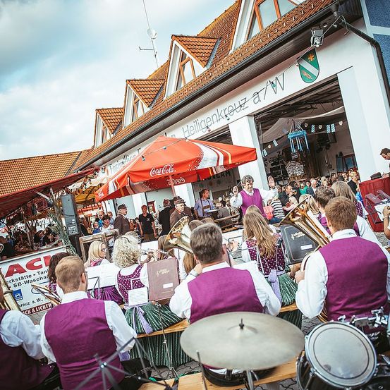 Eine Band spielt im Freien vor einer Menge. Die Musiker tragen lila Westen. Ein Coca-Cola-Regenschirm steht hinter ihnen.