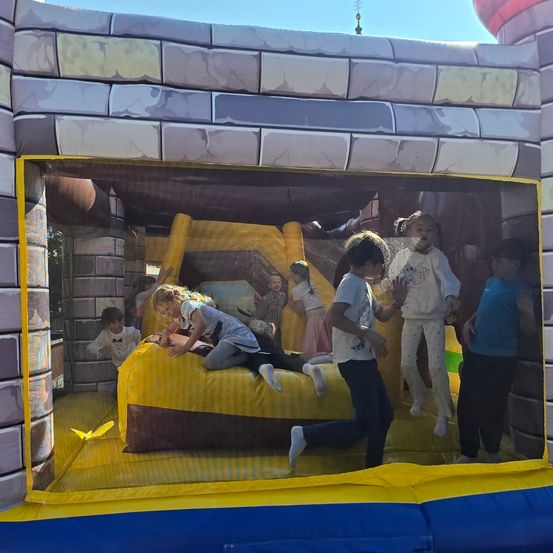 Mehrere Kinder spielen in einem burgartigen Hüpfhaus, eine Mädchen sitzt auf einem Bett und andere stehen herum.