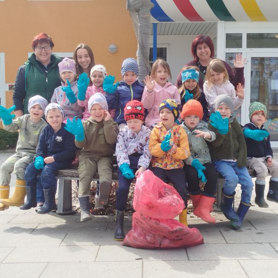Eine Gruppe von Kindern in Winterkleidung posiert für ein Foto vor einem Gebäude. Zwei Frauen stehen auf beiden Seiten von ihnen.