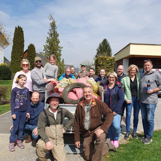 Eine Gruppe von Menschen posiert für ein Foto vor einem Haus mit einem vollgepackten Müllwagen dahinter.