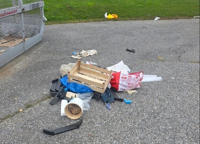 Ein Haufen Abfall, darunter Plastiktüten, ein Holzkisten und andere Gegenstände, liegt auf dem Boden in der Nähe eines Metallkäfigs mit der Nummer 069800.