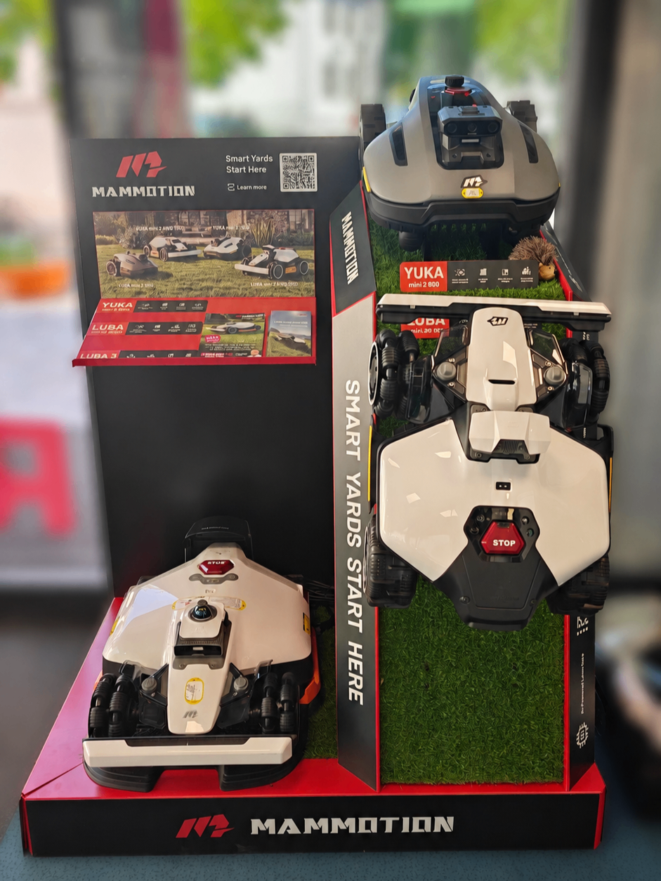 A display of smart lawn mowers, including a model with a red stop button, set against a black background with a QR code and a hedgehog.