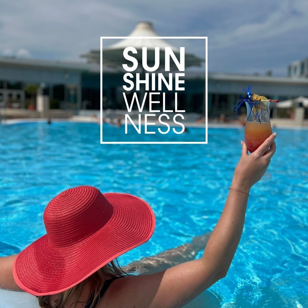 Eine Frau in einem roten Hut hält einen Cocktail in einem Schwimmbad. Die Worte 'SUN SHINE WELLNESS' sind auf einem weißen Hintergrund über ihr angezeigt.