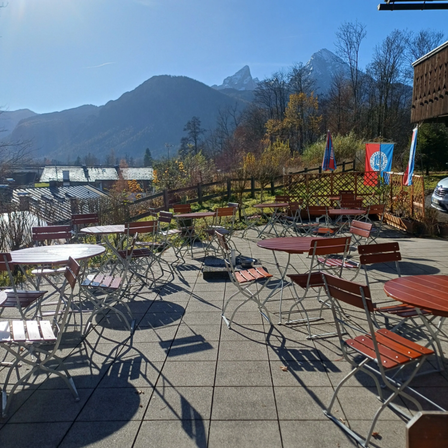 Terrasse eines Restaurants mit Tischen und Stühlen, Blick auf die Berge. Ein klarer Himmel und mehrere Fahnen sind sichtbar.