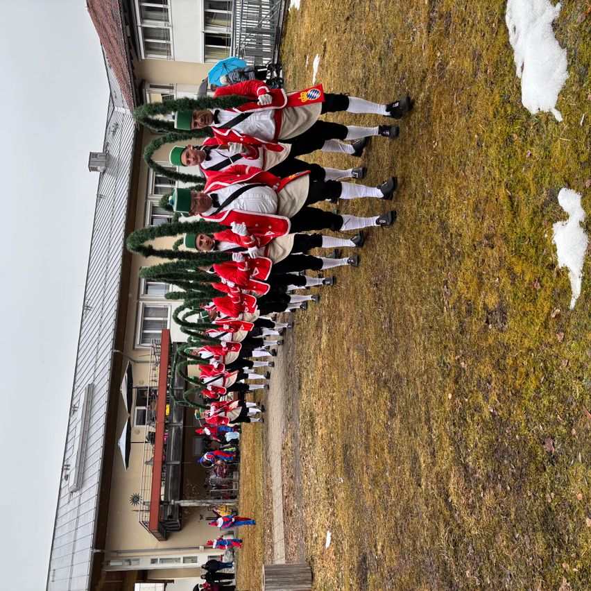 Eine Gruppe von Menschen in roten und weißen Kostümen steht in einer Reihe vor einem Gebäude mit schneebedecktem Dach.