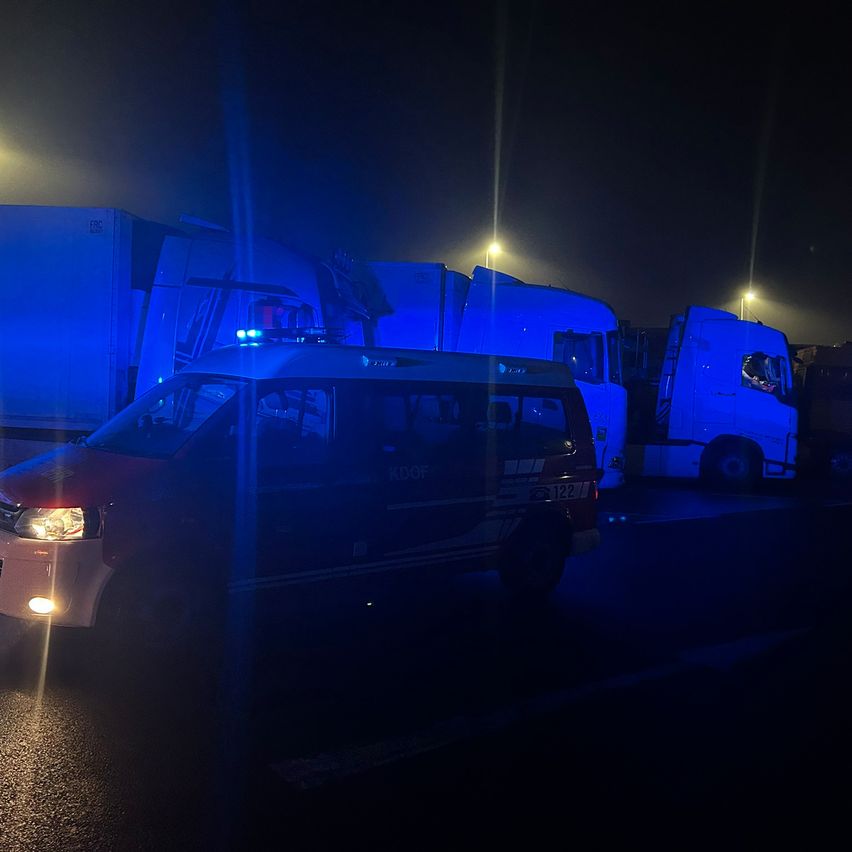 Ein Notfallfahrzeug mit eingeschalteten Lichtern ist vor mehreren Lastwagen in einem dunklen Bereich geparkt.