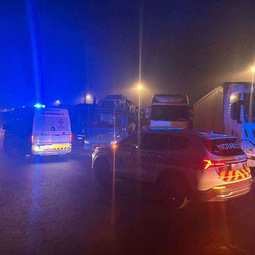 Ein Krankenwagen mit blauen Lichtern ist auf der Straße geparkt. Dahinter sind mehrere Lastwagen in einer Reihe. Ein Polizei-SUV ist vor den Lastwagen geparkt.