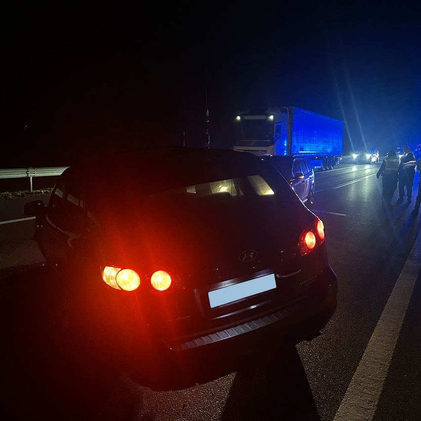 In der Nacht ist ein Auto mit eingeschalteten Rücklichtern am Straßenrand geparkt, möglicherweise von der Polizei angehalten.
