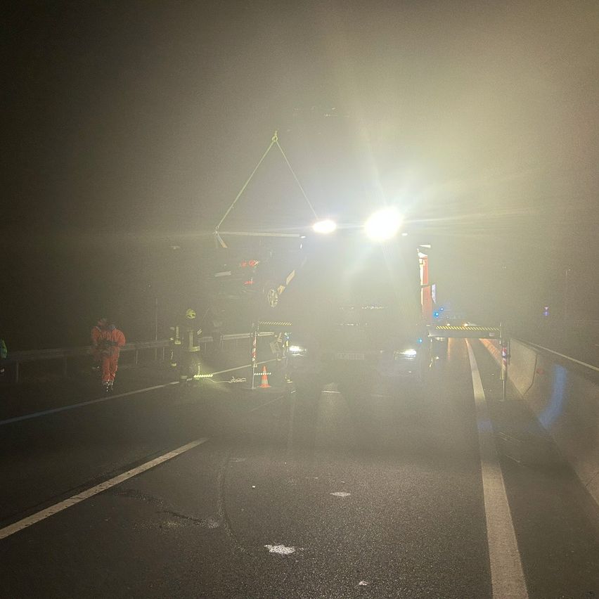 Rettungskräfte arbeiten an einem Fahrzeug bei Nebel. Das Fahrzeug wird von einem Kran angehoben, und um es herum sind Warnbaken aufgestellt.