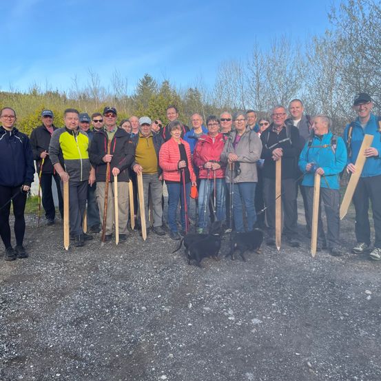 Eine Gruppe von Menschen in Winterkleidung mit Wanderstöcken steht auf einem Schotterweg mit Bäumen im Hintergrund. Sie lächeln und posieren für ein Foto.