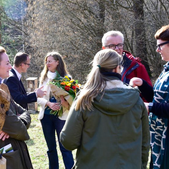 Gruppe von Menschen, die in einem Park stehen. Eine Frau, die einen Blumenstrauß hält, steht in der Mitte.