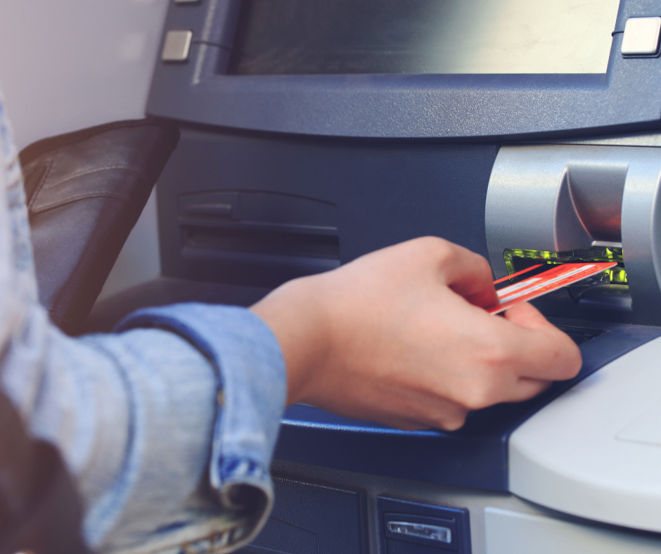 Eine Person steckt eine Kreditkarte in einen Geldautomaten. Die Karte ist rot und weiß.