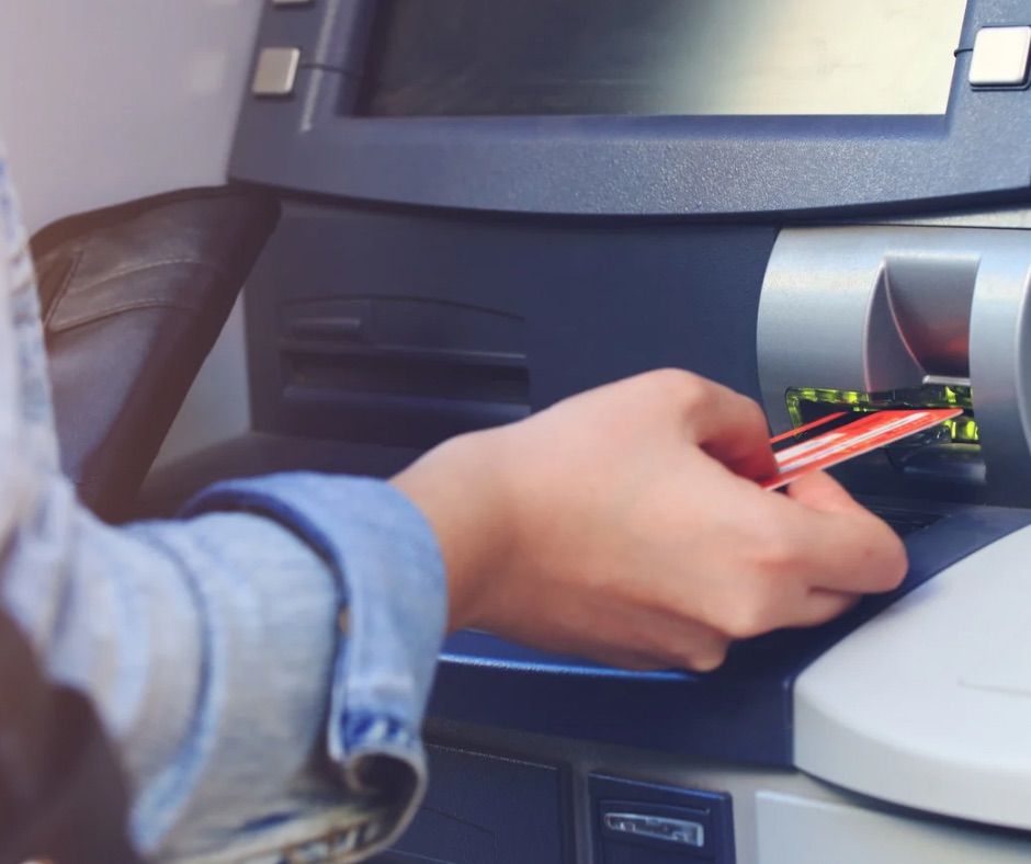 Eine Person steckt eine Karte in einen Geldautomaten. Der Geldautomat ist silber und schwarz. Der Kartenschlitz ist grün.