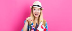 A smiling woman with a hat holds flags of various countries, including the USA, Australia, Germany, and Canada, against a pink background.