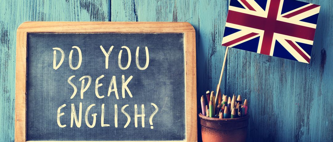 Ein Kreidetafel mit der Frage Do You Speak English darauf, eine kleine Union Jack Flagge und ein Behälter mit farbigen Stiften.