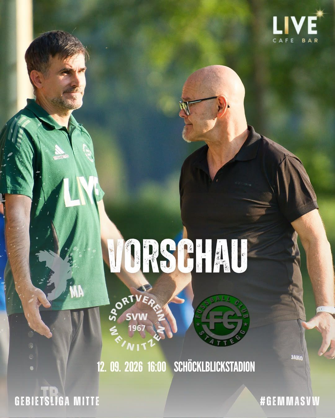 Zwei Männer stehen auf einem Feld, einer trägt ein grünes Shirt mit 'LY' und der andere in Schwarz mit einer Brille. Sie scheinen etwas zu besprechen. Der Hintergrund ist verschwommen mit Bäumen.