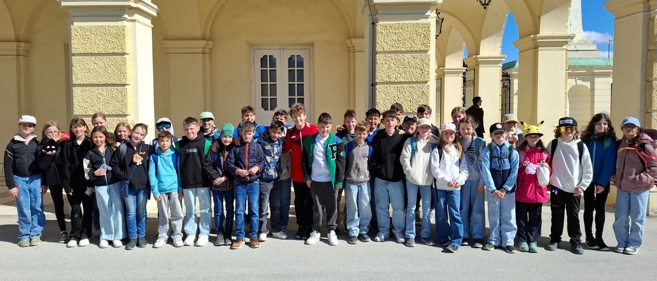 Eine Gruppe von Kindern in Winterkleidung posiert für ein Foto vor einem Torbogen. Der Torbogen hat eine gelbe Wand und einen Eingang mit einer weißen Tür.