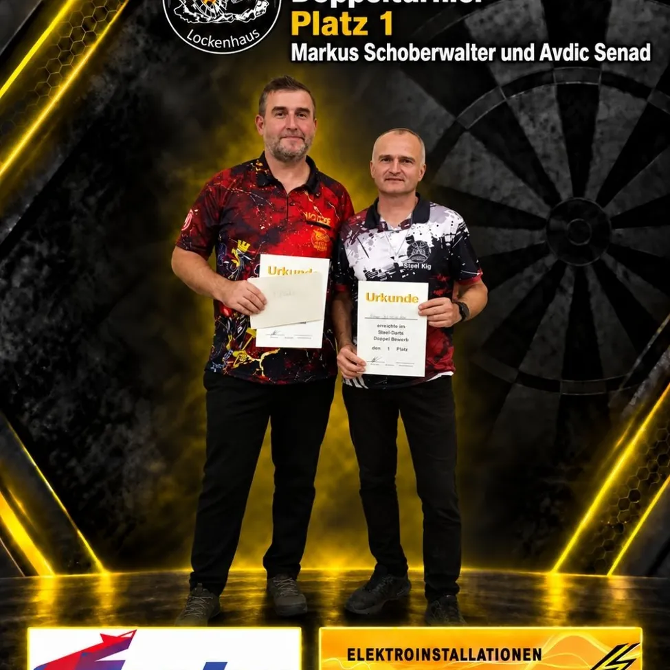 Zwei Männer stehen auf einer Bühne und halten Urkunden in den Händen, einer mit einem roten Shirt und der andere mit einem schwarz-weißen Shirt. Sie stehen vor einem Dartboard-Hintergrund.
