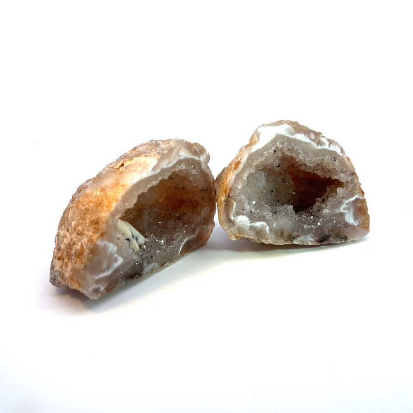 Zwei Geodenhälften mit einer rauen Außenschicht und einem kristallinen Inneren werden auf einer weißen Oberfläche gezeigt.