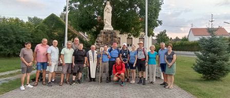 Eine Gruppe von Menschen in Wanderausrüstung, einige mit Hüten, posiert für ein Foto vor einer Statue der Jungfrau Maria.