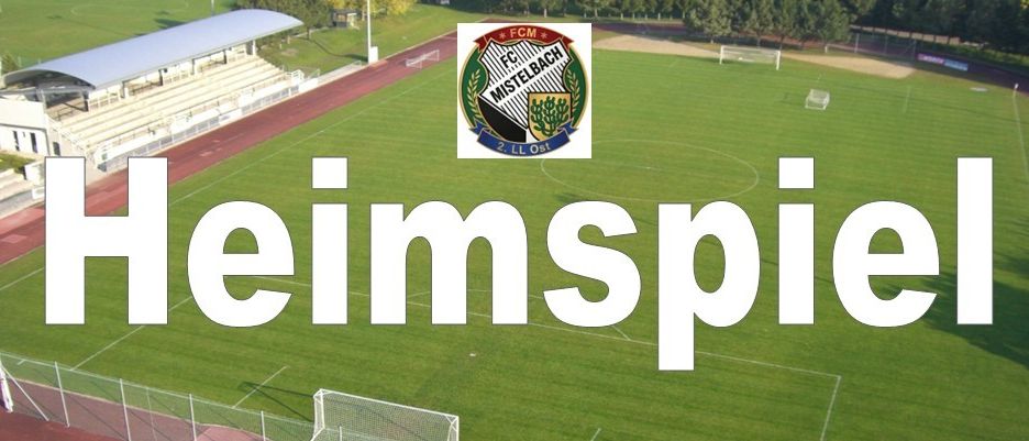 Eine Draufsicht auf ein Fußballfeld mit dem Text 'Heimspiel' in weißer Schrift. Das Feld ist leer, und es gibt ein Logo in der Mitte. Das Feld ist von einem Zaun umgeben, und es gibt Bäume und ein Gebäude in der Ferne.