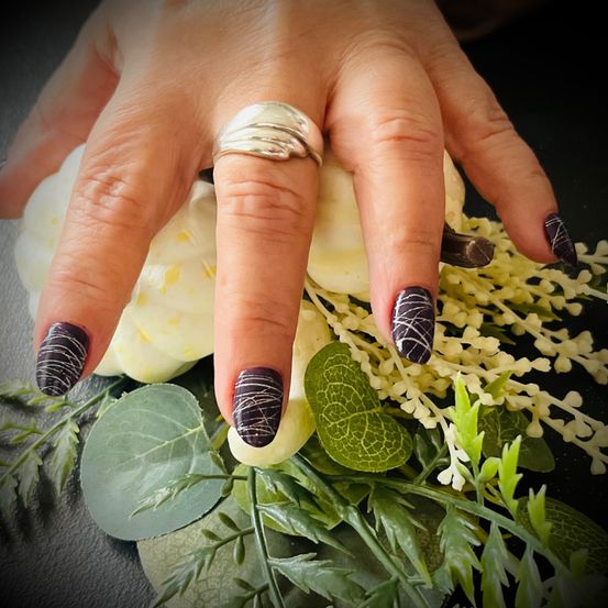 Ein Nahaufnahme einer Hand mit schwarz-weißem Nageldesign über einer Blumenanordnung. Die Nägel haben einen marmorierten Effekt und ein silberner Ring ziert den Mittelfinger.
