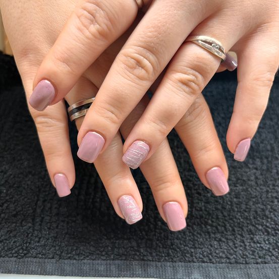 Nahaufnahme von zwei Händen mit hellem rosa Nagellack, einer mit einem Diamantring und der anderen mit einem silbernen Ring.