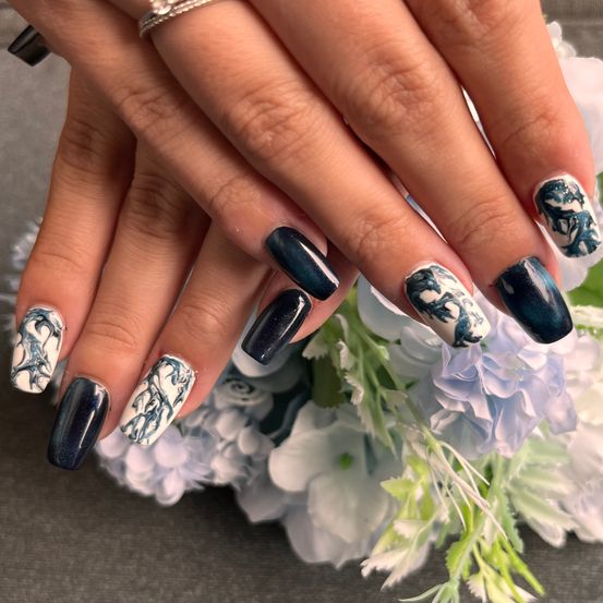 Ein Nahaufnahme von Händen mit blauer und weißer marmorierter Nagelkunst, einem Ring und einem Strauß weißer und lila Blumen im Hintergrund.