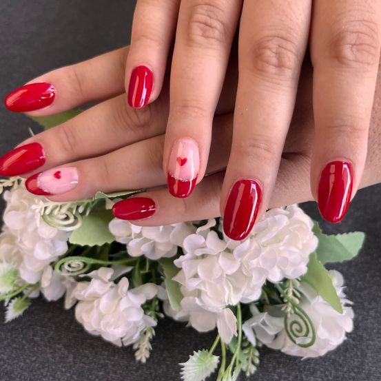 Ein Nahaufnahme von zwei Händen mit rotem, herzförmigem Nagellack auf weißem Blumenhintergrund. Die Nägel sind gepflegt und lackiert.