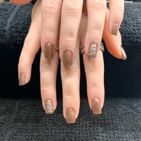 Ein Nahaufnahme der Hände einer Person mit braunen, polierten Nägeln und zwei Ringen am Mittelfinger und am Ringfinger.