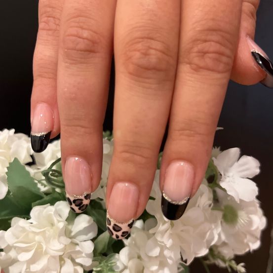 Eine Hand mit Nägeln, die in Schwarz und Pink lackiert sind, mit Leoparden-Print-Designs auf einigen von ihnen. Die Nägel sind von weißen Blumen umgeben.