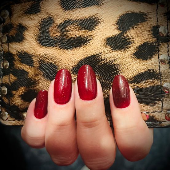 Eine Nahaufnahme einer Hand mit rotem, glitzerndem Nagellack auf einem Hintergrund mit Leopardenmuster-Tasche.
