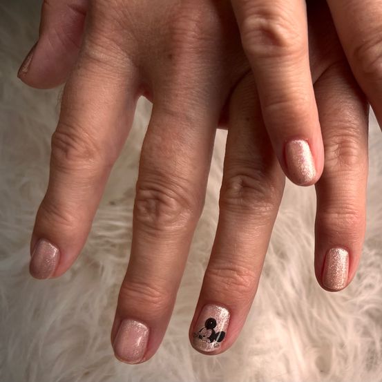 Nahaufnahme der Hände einer Person mit in Pink und Gold lackierten Nägeln, die Mickey-Mouse-Designs aufweisen.