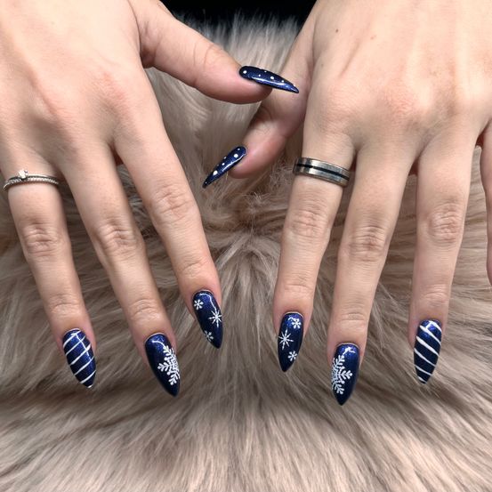 Zwei Hände mit blauer und weißer Nagellackierung mit Schneeflockendesigns auf einer weißen Pelzoberfläche. Eine Hand hat einen Ring mit silbernem Band.