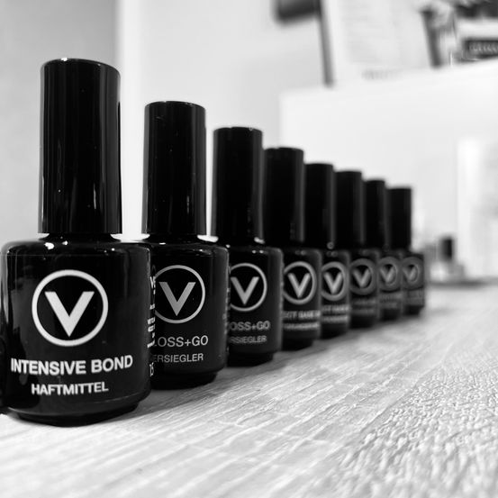 Eine Reihe schwarzer Nagellackflaschen mit dem Markennamen 'V' steht auf einem Holztisch.