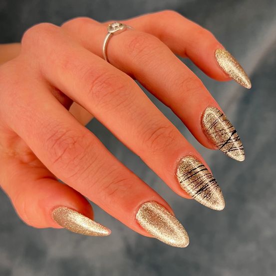 Eine Hand mit goldener, komplizierter Nagelkunst, die vor einem verschwommenen Hintergrund präsentiert wird. Jeder Nagel hat ein einzigartiges Design.