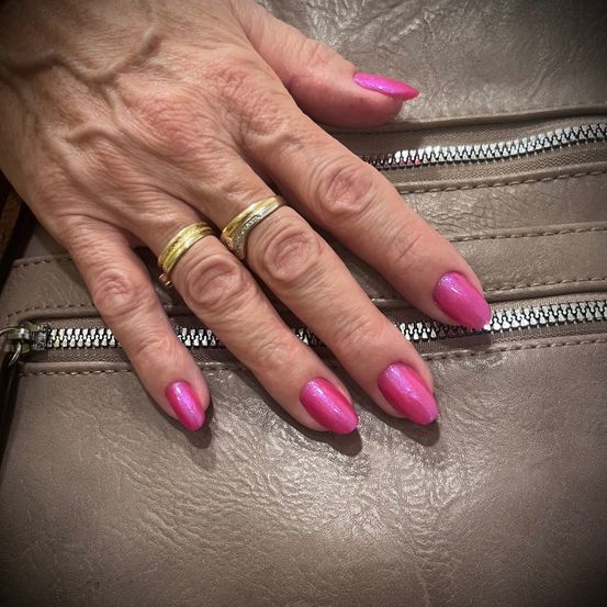 Eine Nahaufnahme einer Hand mit rosa Nägeln auf einer braunen Ledertasche. Die Nägel sind ordentlich gepflegt, und zwei goldene Ringe sind an den Fingern zu sehen.