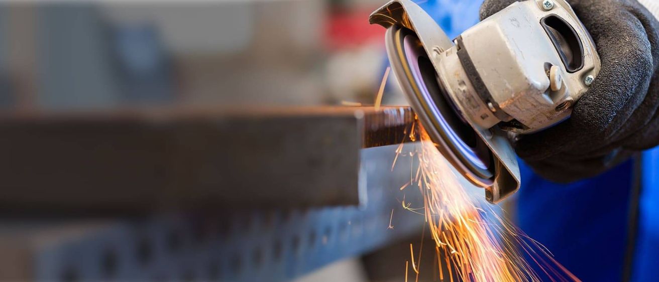 Ein Metallschleifer schneidet ein Metallblech und erzeugt Funken. Der Schleifer und das Blech sind metallisch.