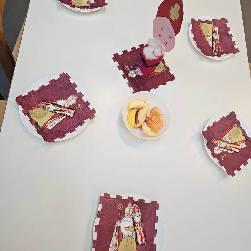 Ein Tisch mit sieben Tellern, jeder mit einer Serviette, einer Figur von Santa Claus und einer kleinen Schüssel mit Obst. Der Tisch ist weiß, und der Raum ist schwach beleuchtet.