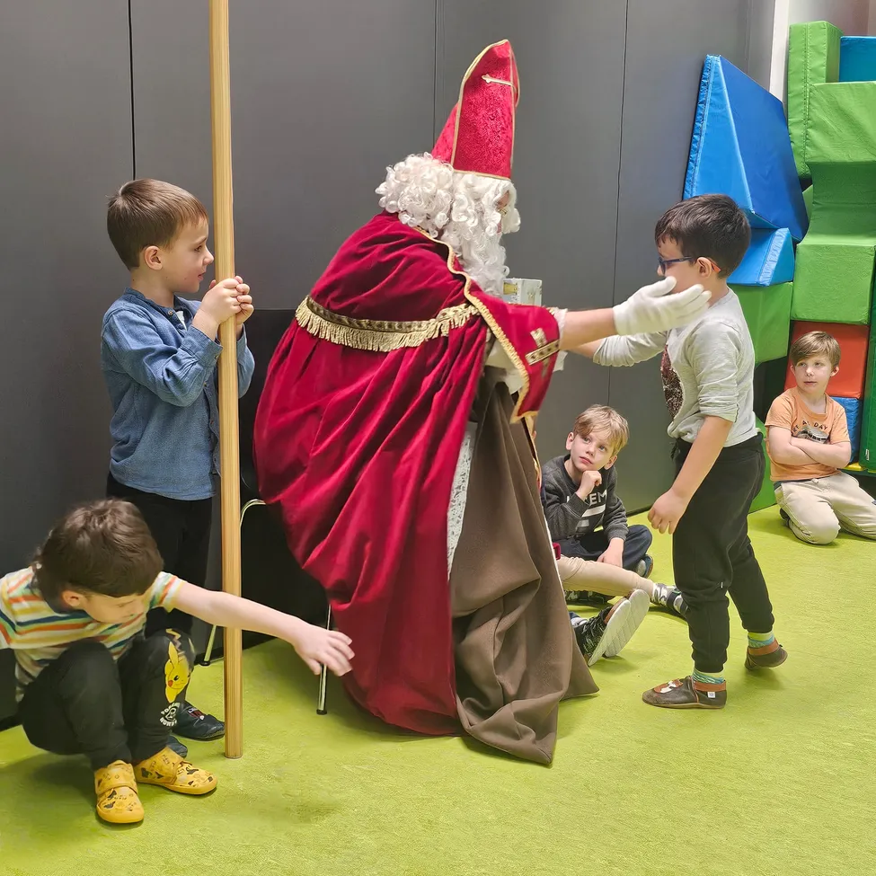 Eine Gruppe von Kindern sitzt und steht um einen als Weihnachtsmann verkleideten Mann herum. Er verteilt etwas an die Kinder.