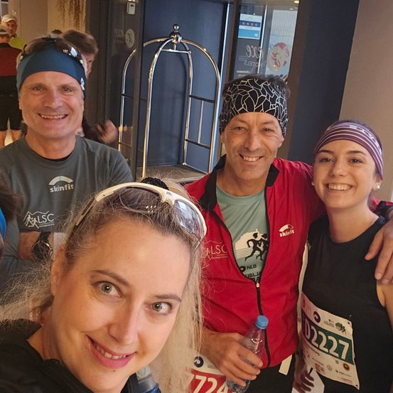 Eine Gruppe lächelnder Menschen, wahrscheinlich ein Marathon-Team, mit Stirnbändern, Sonnenbrillen und einer Wasserflasche.