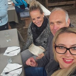 Eine Frau mit einem schwarzen Schal lächelt und posiert für ein Foto mit zwei Männern, die eine Brille tragen.